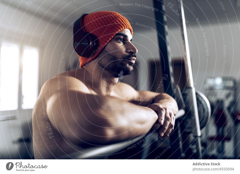 Shirtless man adjusting headphones before training with barbell athlete muscular abs strong workout listen male sportsman naked torso music power wellness