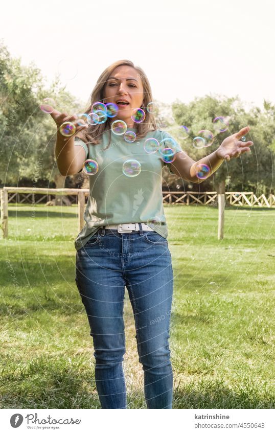 Women playing with soap bubbles in a park adult Middle aged women t-shirt smile magic casual happy fun green grass mock up Outdoor sunny fair haired millennial