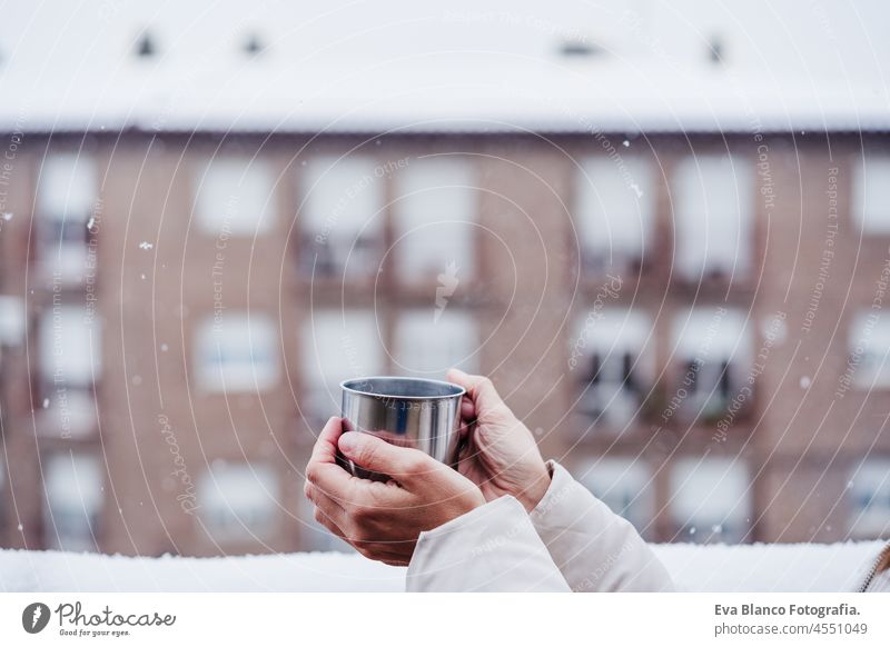 side view of happy woman on terrace at home enjoying cup of hot coffee, neighborhood background. Snow in the city winter snow smoke snowing metallic tea