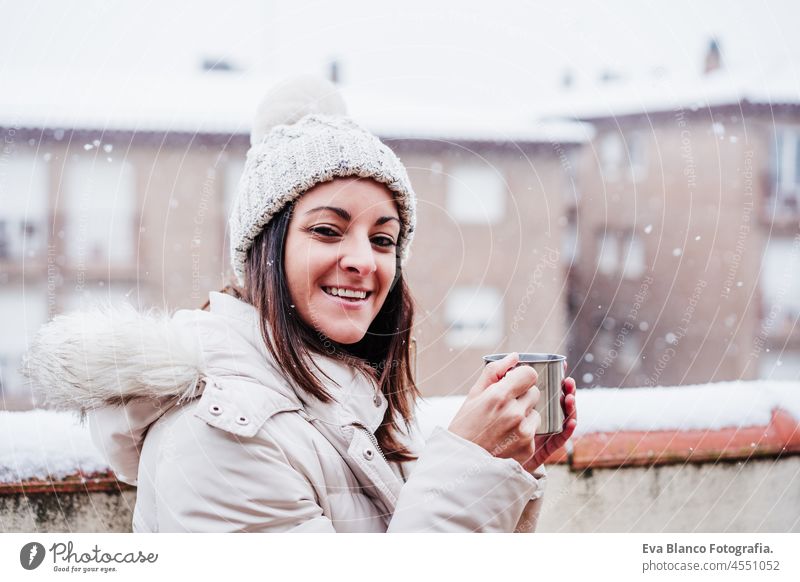 happy woman on terrace at home enjoying cup of hot coffee, neighborhood background. Snow in the city winter snow smoke snowing metallic tea beverage sofa wooden