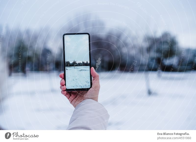 unrecognizable woman hand taking picture with mobile phone to snowy landscape during winter season. screen device photographer cold coat close up internet
