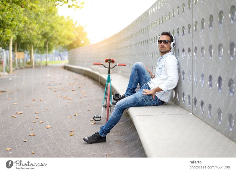 Young man biker relaxing on a bench while listening music person cool electronic guy latin mobile phone one person outside radio stylish boy cycle male riding