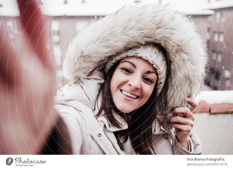 happy woman on terrace at home enjoying snow while taking selfie with mobile phone, neighborhood background. Snow in the city winter photographer friends