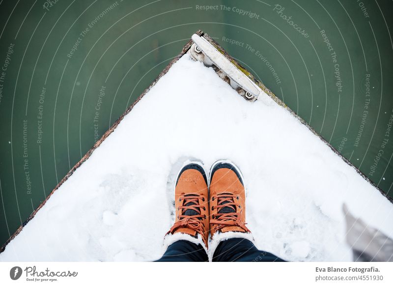 top view of unrecognizable female feet boots standing on snowy pier by frozen lake during winter. hiking concept footprint equipment brown modern walking woman