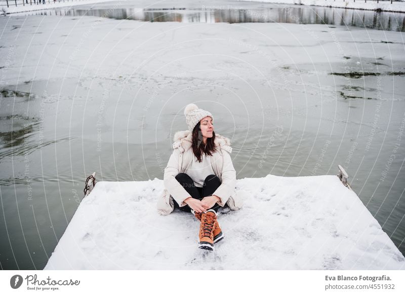 happy woman with eyes closed sitting on pier in front of frozen lake in city. travel and Lifestyle during winter in city snow landscape relaxing frost backpack
