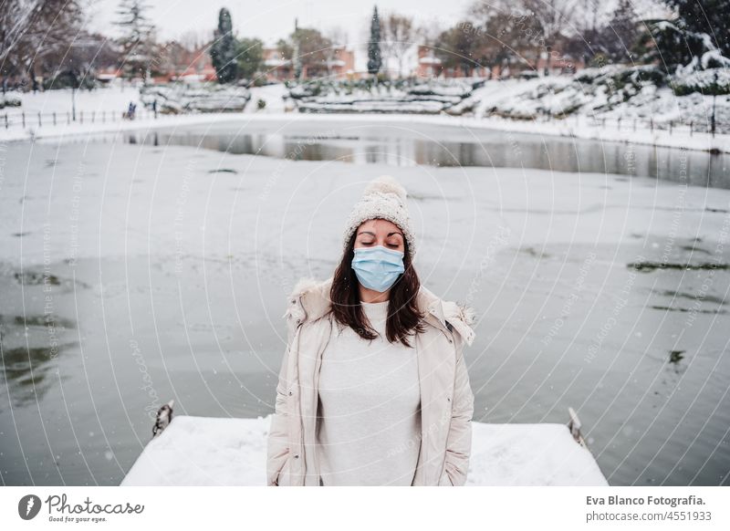 relaxed woman with eyes closed wearing face mask standing on pier in front of frozen lake in city. travel and Lifestyle during winter in city during pandemic corona virus