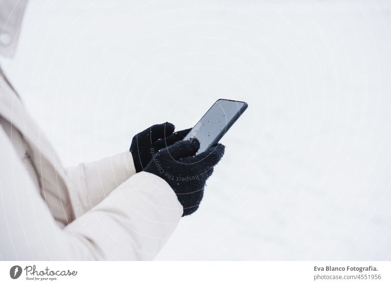 unrecognizable woman walking outdoors in city during winter while snowing, using mobile phone.winter lifestyle technology internet online smart phone screen
