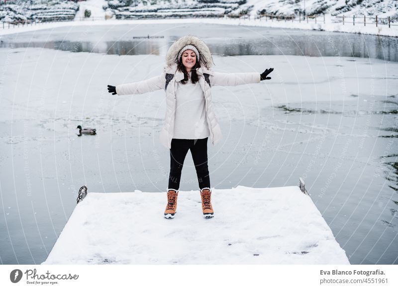 happy caucasian woman with eyes closed and arms outstretched standing on snowy pier during winter by frozen lake. Winter lifestyle in nature portrait hood calm
