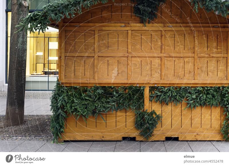 closed christmas sales stand made of wood decorated with fir greenery in a shopping street of the city centre / anticipation / corona ordinance sales booth