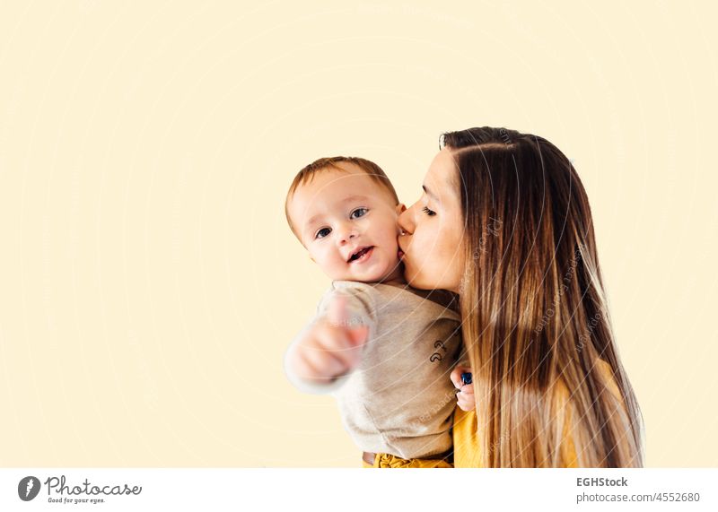 Portrait of young business woman kissing her baby boy in yellow background mom work family empower busy mother office career super empowered child happy kid