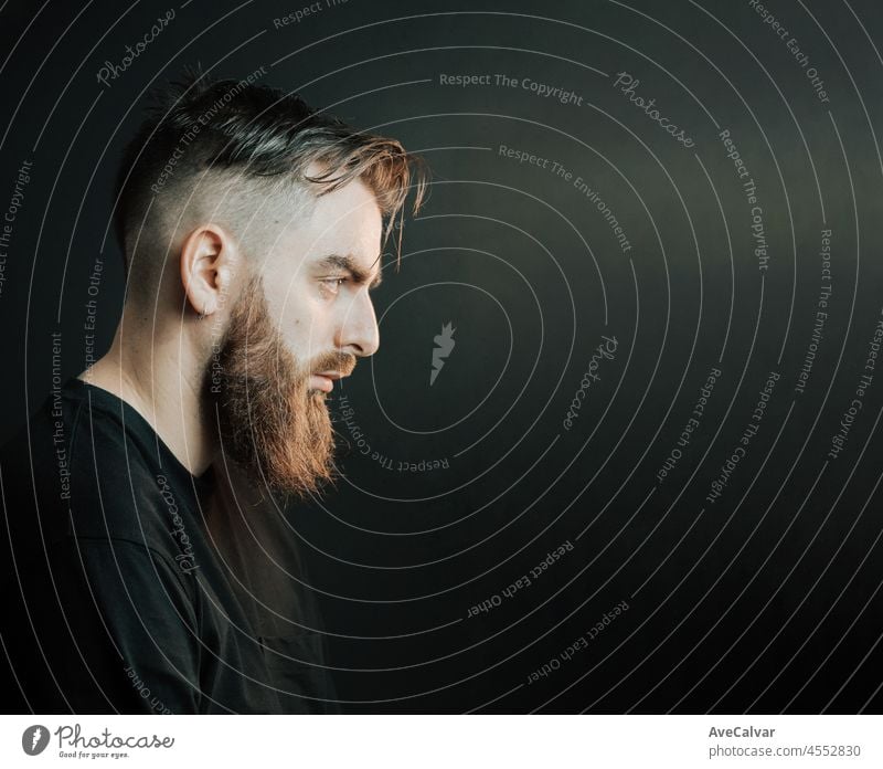 Cinematic portrait side view of a young hipster bearded man with copy space with cinematic lighting. Attractive man looking serious straight to camera, mental health concept. Depression and anxiety