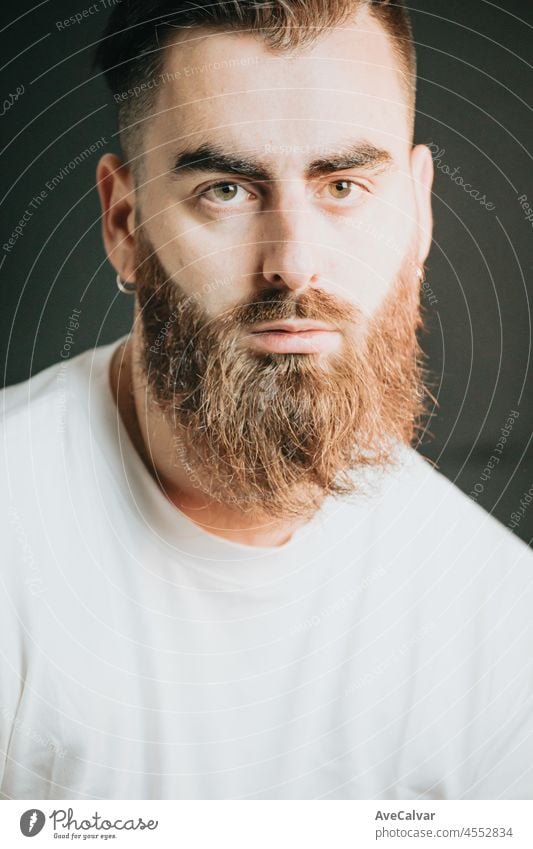 Cinematic shot of a young hipster bearded man with modern hairstyle with cinematic lighting. Attractive man looking serious straight to camera, mental health concept. Depression and anxiety portrait