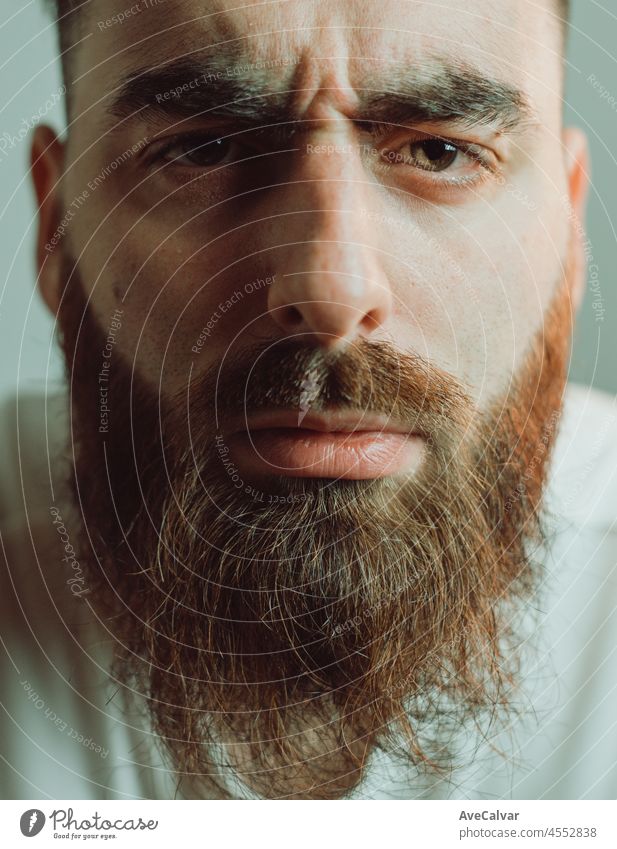 Portrait of a young bearded man looking very close to the lens. Funny image of a young man inspecting something. Cinematic tones and lightning. mental health concept, depression and anxiety
