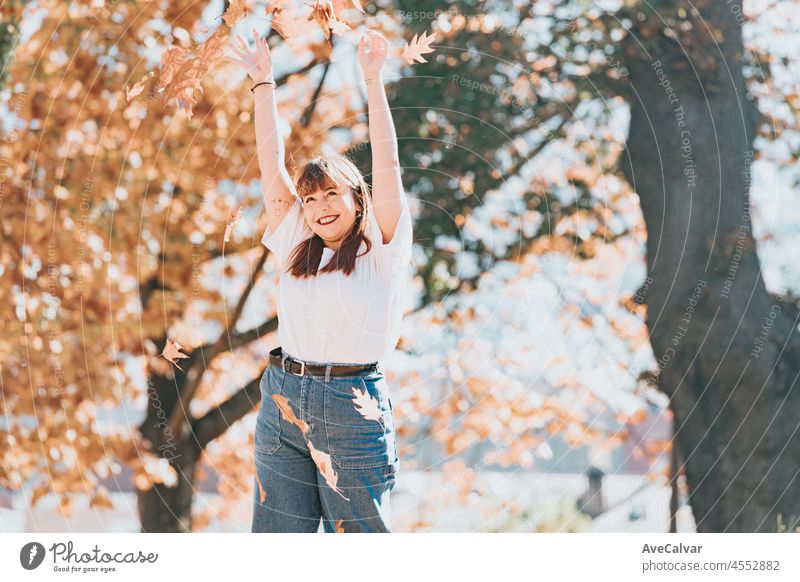 Happy young woman having fun in autumn forest.Woman portrait. Happy girl in white shirt and blue jeans is playing with leaf, looking at camera and smiling. Copy space.Portrait in autumn park.