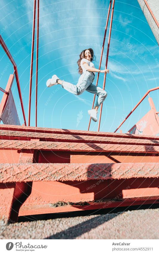 Urban image of a young woman with long hair jumping in the sky, wide angle shot. Modern outfit white shirt blue jeans white shoes. City life style. Liberty and freedom concept