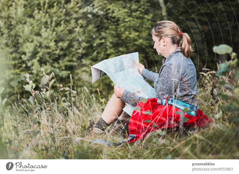 Woman with backpack having break during trip in mountains looking at map sitting on grass summer active woman adventure activity fun travel trekking vacation