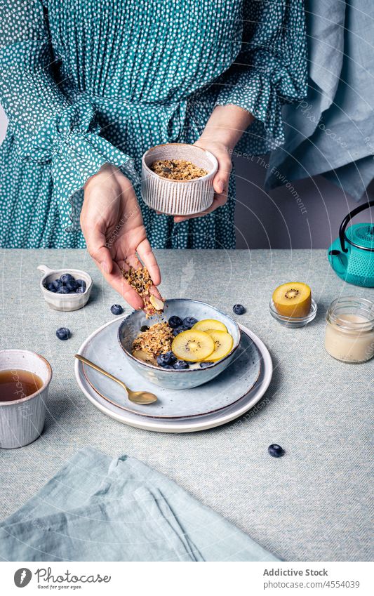 Woman adding granola to bowl with fruit woman blueberry kiwi food breakfast nutrition portion morning female tea homemade muesli ingredient healthy food spoon