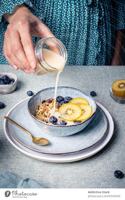 Woman pouring milk into bowl with granola woman cereal kiwi breakfast blueberry vitamin homemade female meal morning dairy add appetizing healthy food plate