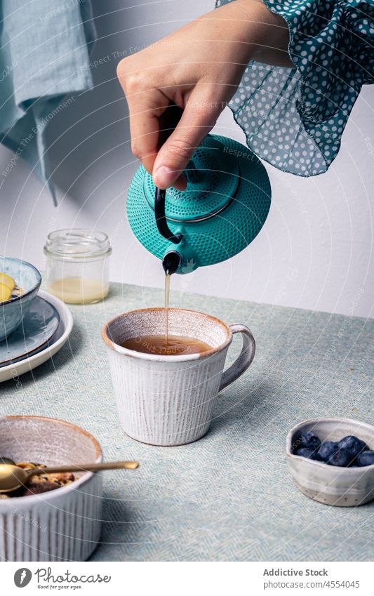 Woman pouring hot tea for breakfast woman granola kiwi food blueberry prepare healthy female tasty nutrition serve sweet vitamin hot drink cup fruit spoon table