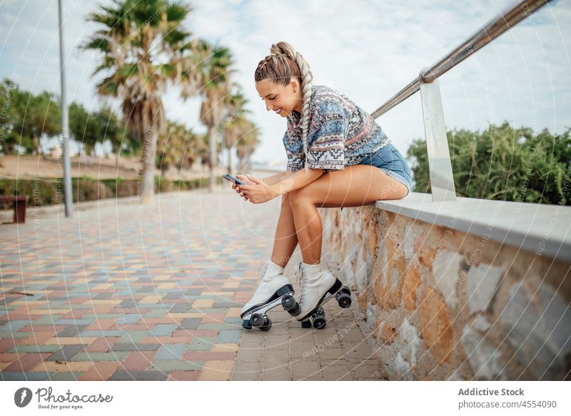 Cheerful roller skater browsing smartphone woman street sportive hobby sidewalk healthy lifestyle online cellphone internet text message positive glad optimist