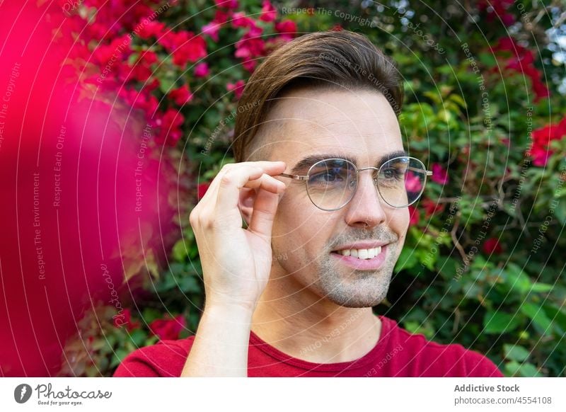 Smiling man against blooming bush in garden positive portrait shrub flower eyeglasses personality glee enjoy male toothy smile glad happy content vegetate