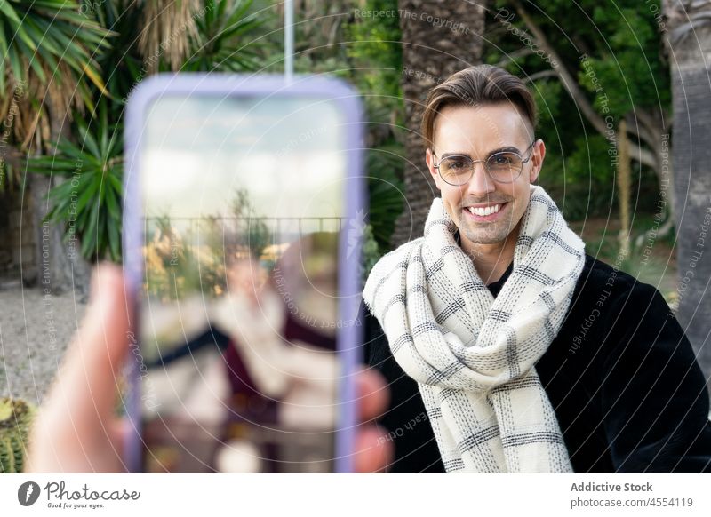 Crop person photographing smiling friend on smartphone man take photo smile garden tropical positive self assured together park confident style male young