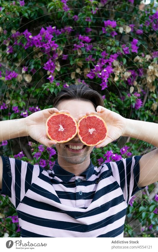 Cheerful guy making eyes with grapefruit and smiling in blooming garden man smile cover eyes joy having fun positive delight cheerful citrus male young brunet