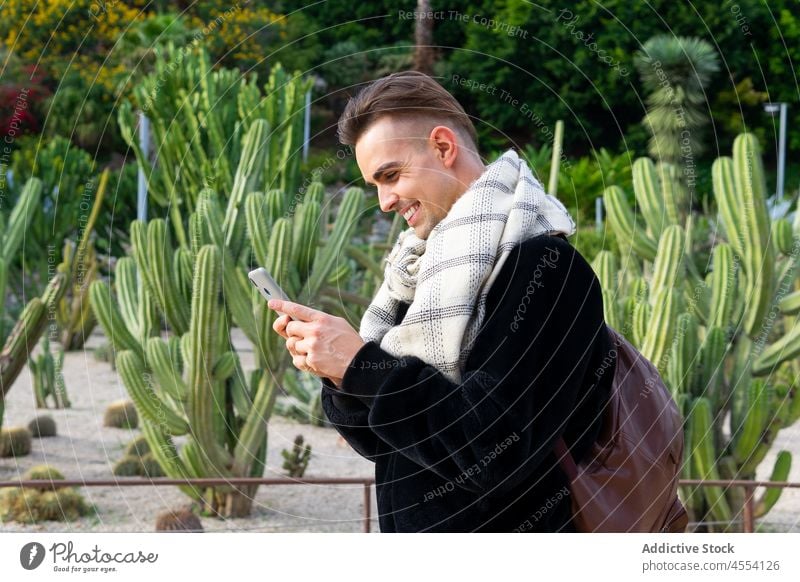 Positive trendy guy browsing smartphone in exotic garden man using smile positive tropical park charismatic fashion railing male young style confident mobile