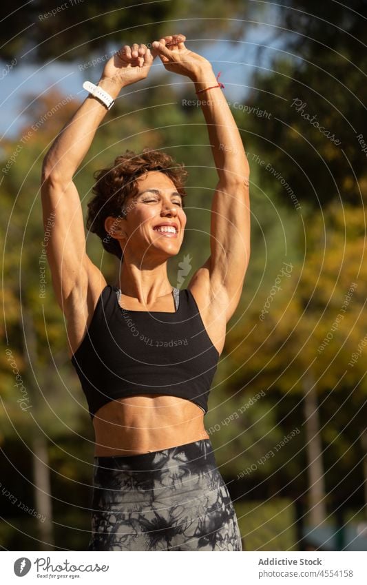 Smiling fit Hispanic lady warming up before training in park sportswoman warm up smile stretch exercise eyes closed workout healthy positive wellness female