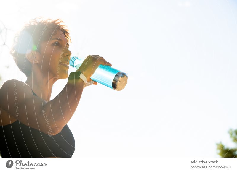 Positive Hispanic sportswoman drinking water during morning workout in park smile training athlete healthy hydrate muscular fitness female adult ethnic hispanic