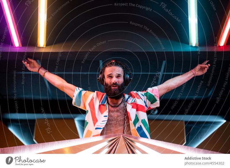 Content bearded DJ standing in club with outstretched arms during party man dj nightclub self assured content perform music sound confident modern male young