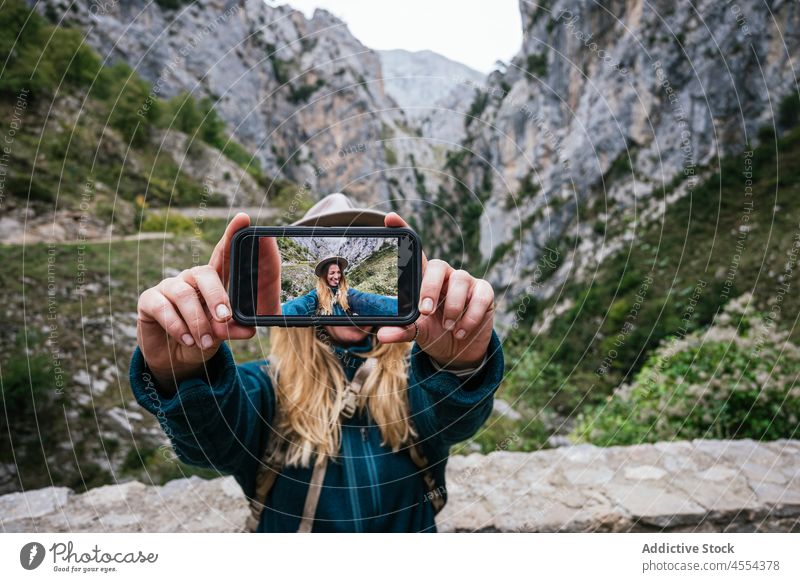Playful woman taking selfie with smartphone during hike in mountains explorer using wink grimace trekking female rock show tongue environment rocky vacation