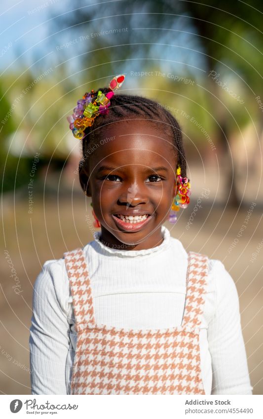 Happy black kid smiling at camera standing in park in sunlight child smile happy nature style portrait childhood cheerful joy girl positive adorable glad