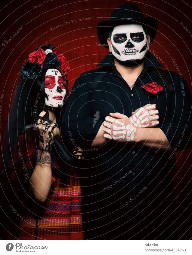 beautiful woman with a sugar skull makeup with a wreath of flowers on her head and a skeleton man in a black hat holding a gun adult art beauty bone bride