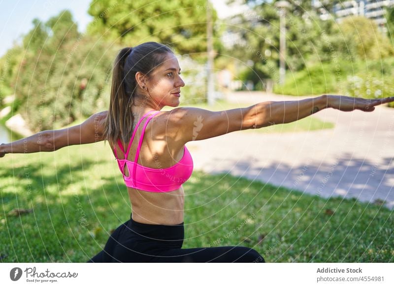 Woman doing warrior pose in park woman training exercise asana pilates lawn practice female yoga activewear Virabhadrasana sportswear wellbeing fit activity