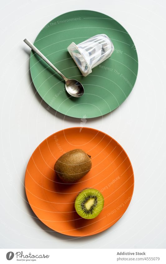Ripe healthy kiwi with yogurt and spoon served on multicolored plates fruit vitamin fresh ripe minimal ceramic table halved food tasty delicious raw snack