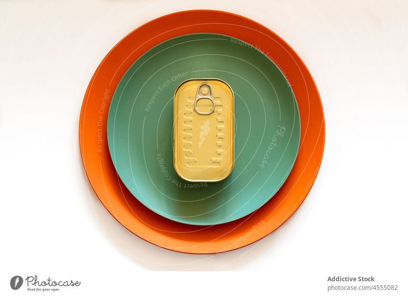 Closed metal can placed on two colored plates on table tin close canned food container tasty preserve dish delicious aluminium snack yummy simple meal sprat