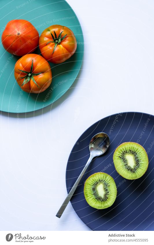 Ripe kiwi and tomatoes placed on colored ceramic plates on table vitamin fresh fruit vegetable healthy food natural ripe vegan organic halved whole tasty exotic