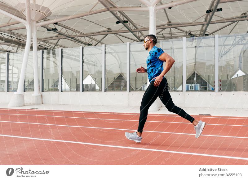 Fit man with sportswear and sunglasses running on the field track handsome male ethnic african young adult athlete runner training exercising fitness exercise