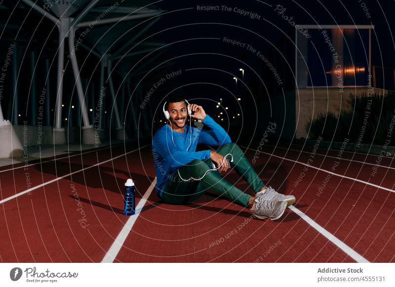 Athlete using phone and listening music on the floor of the running track young man male african confident handsome athlete smart phone headphones