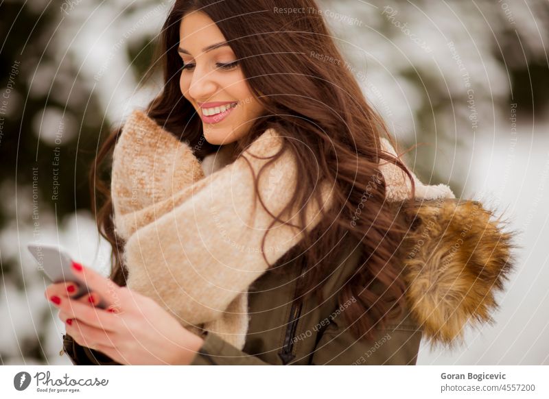Smiling young woman with cell phone in winter outdoors attractive beautiful casual caucasian cellphone cellular cold communication female freeze happy lifestyle
