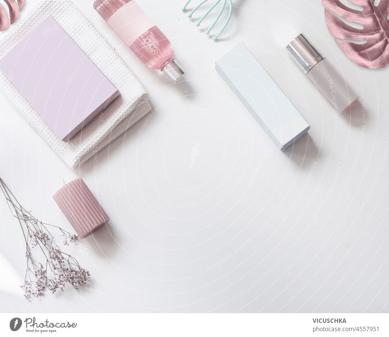 Beauty background with various cosmetic products, spray bottles, boxes and pink leaves on white table. Pink and white cosmetic concept with empty label mock up. Top view with copy space.