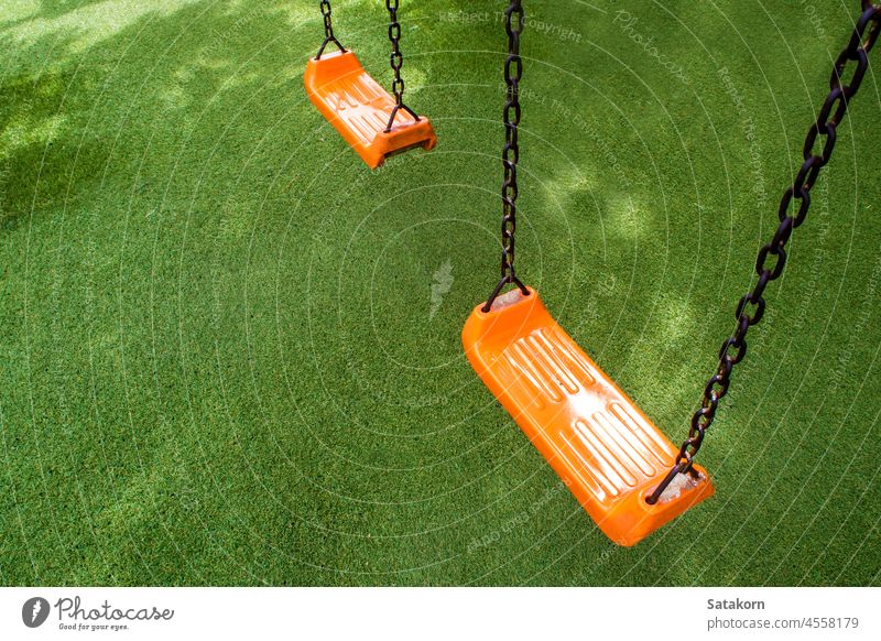Swing seat on the artificial grass playground swing child orange color plastic park fun outdoor childhood school recreation toy green colorful object activity