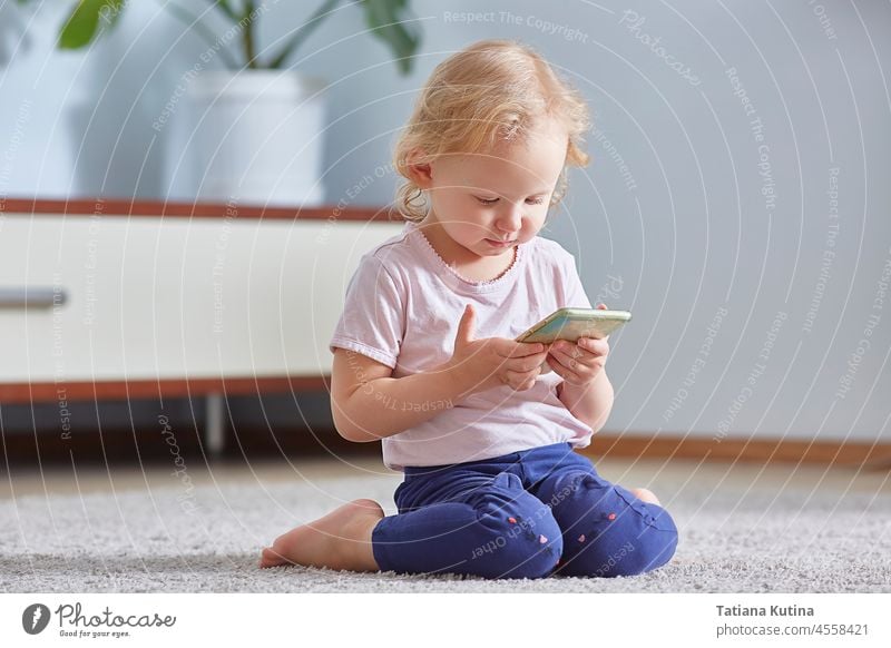 child girl look smart phone and sits on the gray carpet in living room. Child development Concept. technology mobile kid telephone smartphone screen play happy
