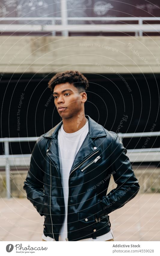 Ethnic guy standing on street near fence man portrait thoughtful confident wistful pensive railing hand in pocket ponder think leather jacket african american
