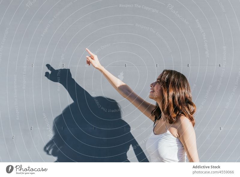 Brunette pointing up on gray background woman point up indicate attention index finger show gesture sign wall content smile cheerful expressive delight positive