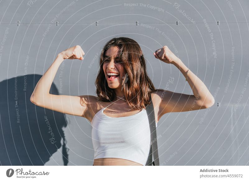 Happy lady doing winner gesture near gray wall woman portrait cheerful arms raised success clench fist celebrate triumph glee victory expressive delight