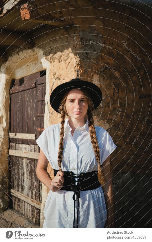 Young female with braids standing near old stone building woman confident belt street wall portrait accessory leather serious dress door metal house wooden