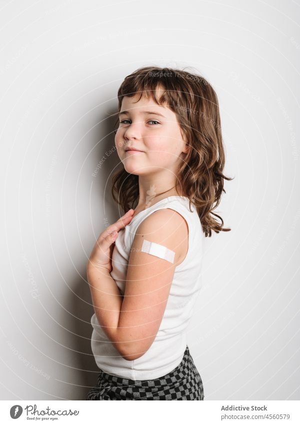 Serious vaccinated girl with band aid on arm schoolgirl bandage vaccine protect virus vaccination jab happy smile shot safety health care medical healthy