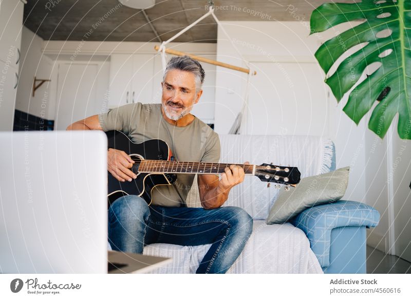 Elderly guitarist performing music on sofa near laptop man musician loft instrument interior acoustic play online headphones chill couch meloman aged hobby